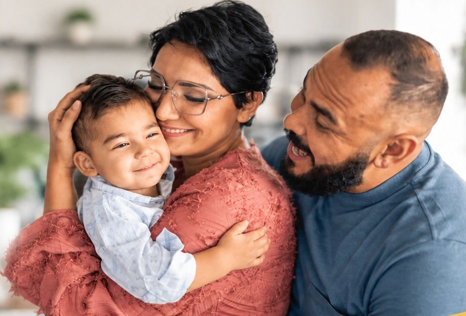 A couple embraces their young son in the living room.